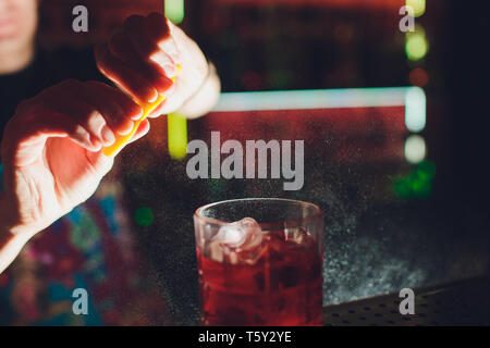 Les mains de barman en saupoudrant l de jus dans le verre à cocktail rempli de boisson alcoolisée sur le fond sombre. Banque D'Images