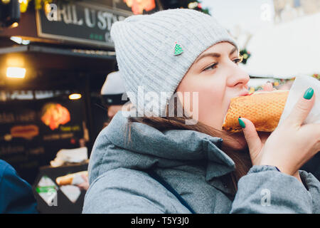 Closeup portrait de femme de la faim dans les verres eating hot dog à l'extérieur arrière-plan. Banque D'Images