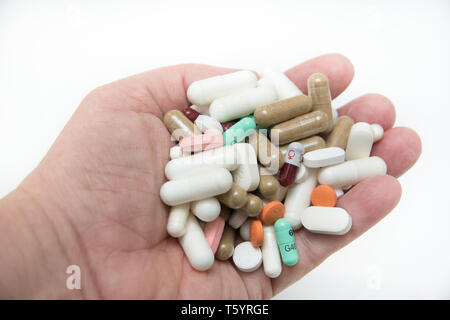 Une main tenant une grande quantité de médicaments - médicaments en comprimés, sous forme de comprimés et gélules sur un fond blanc. Banque D'Images