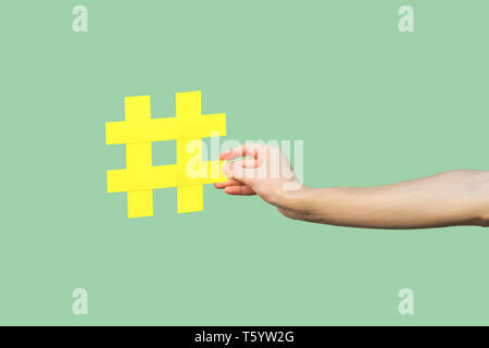 Social media concept, closeup portrait of hand holding large big yellow hash tag signe. Piscine, isolée, copy space, fond vert, marketing symbo Banque D'Images