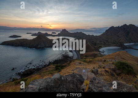 Femme fait une randonnée le long des sommets des crêtes des îles de Komodo alors que le soleil se couche derrière les montagnards lointains Banque D'Images