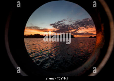 Rivage de l'île de Komodo et spectaculaire ciel de coucher de soleil coloré vu à travers la fenêtre du hublot de fa Boat Banque D'Images