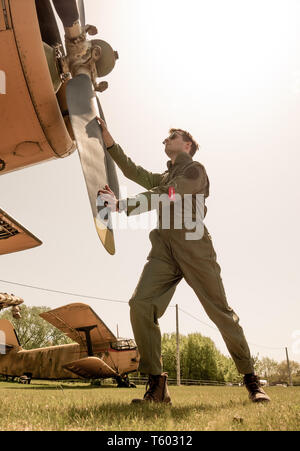 Un beau jeune homme pilote dans un ensemble vert debout à côté de l'hélice d'un vieil avion sur une journée ensoleillée. Banque D'Images