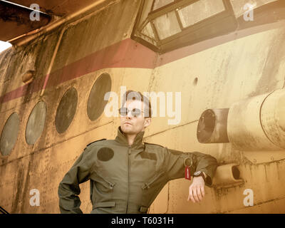 Un beau jeune homme pilote dans un ensemble vert debout à côté d'un vieil avion sur une journée ensoleillée. Banque D'Images