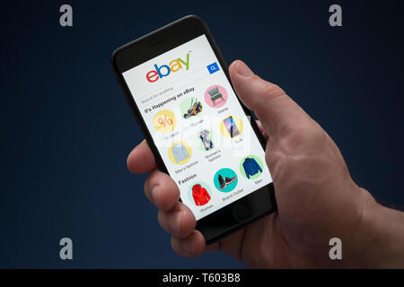 Un homme se penche sur son iPhone qui affiche le logo ebay (usage éditorial uniquement). Banque D'Images