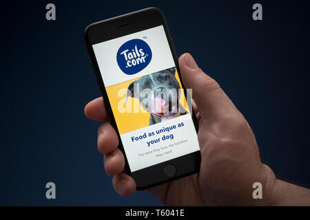 Un homme se penche sur son iPhone qui affiche le logo d'Tails.com (usage éditorial uniquement). Banque D'Images