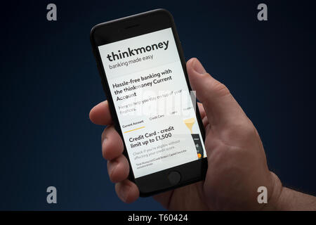 Un homme se penche sur son iPhone qui affiche le logo d'Thinkmoney (usage éditorial uniquement). Banque D'Images