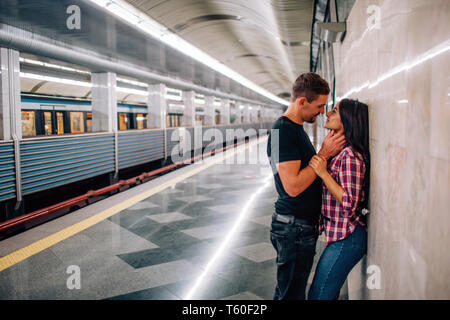 Jeune homme et femme utiliser sous terre. Couple dans le métro. Paasionate joyeux les gens se pencher pour mur. s'embrasser. Guy tenir la main sur son cou. Histoire d'amour. M Banque D'Images