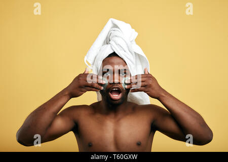 Jeune homme sérieux avec crème anti de vieillissement sur le visage regardant la caméra . guy bouche grande ouverte avec l'application de peinture de guerre sur le visage Banque D'Images