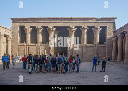 Edfou, Egypte : les touristes écouter leur guide dans la cour du temple d'Edfou, le plus grand temple dédié à Horus et Hathor de Dendérah. Banque D'Images