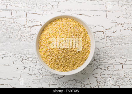 Pile de millet d'or, une des céréales sans gluten, dans un bol blanc sur fond de table blanc rustique haut Vue de dessus Banque D'Images