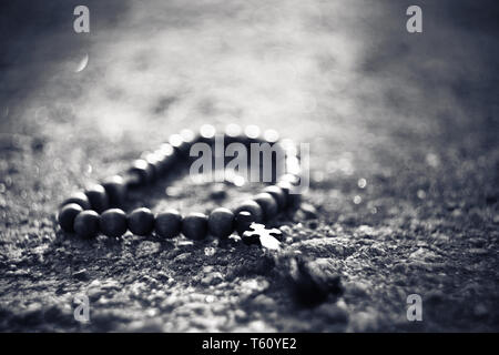 Image en noir et blanc traditionnel en bois de chapelet avec une croix qui se situent sur une surface rocheuse éclairée par une lumière vive. Banque D'Images