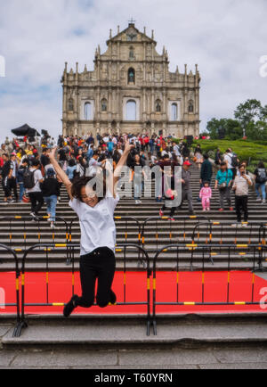 Novembre 2018 - Macao, Chine : Young Asian woman posant pour une photo de saut devant les ruines de St Paul's dans une grande masse de touristes chinois Banque D'Images