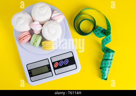 Mètre à ruban vert, balance de cuisine numérique avec ses macarons et meringues sur fond jaune. La perte de poids et le traitement minceur concept. Vue d'en haut Banque D'Images