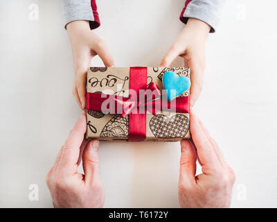 Les mains de l'enfant et l'adulte man's hands, superbe boîte cadeau, ruban et enrobée de cookies sur un fond de bois, blanc. Vue de dessus, close-up. La préparation pour le th Banque D'Images