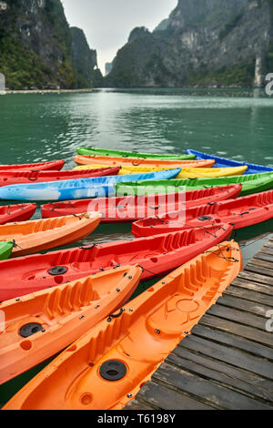 De nombreux kayaks colorés sur la jetée en bois sur les roches vertes en fond de la Baie d'Halong au Vietnam. Ils sont de couleur orange, rouge, bleu, jaune et vert. Libre. Banque D'Images