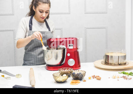 Jeune femme pâtissier bat la crème dans un bol en métal rouge dans un mélangeur électrique. Le concept de pâtisserie maison, la cuisine. Banque D'Images