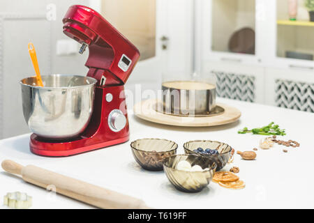 Jeune femme pâtissier bat la crème dans un bol en métal rouge dans un mélangeur électrique. Le concept de pâtisserie maison, la cuisine. Banque D'Images
