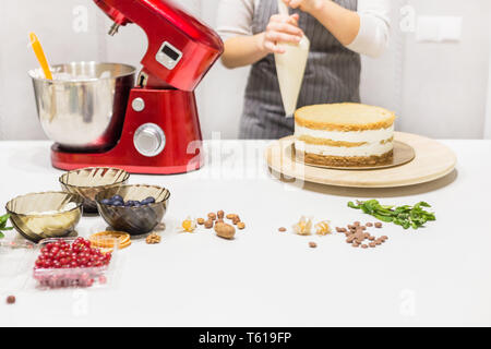 Jeune femme pâtissier bat la crème dans un bol en métal rouge dans un mélangeur électrique. Le concept de pâtisserie maison, la cuisine. Banque D'Images