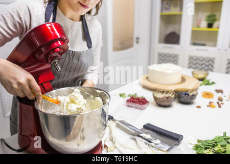 Jeune femme pâtissier bat la crème dans un bol en métal rouge dans un mélangeur électrique. Le concept de pâtisserie maison, la cuisine. Banque D'Images