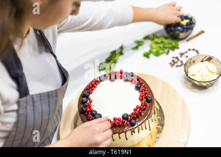Pâtissier décore avec des baies un biscuit gâteau au chocolat blanc et crème. Cake se dresse sur un support en bois sur un tableau blanc. Le concept de Banque D'Images