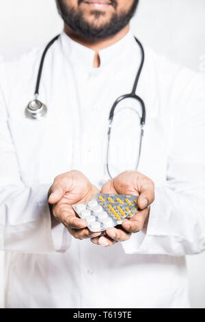 Beau jeune médecin dans une robe blanche avec un stéthoscope détient sur une main tendue un comprimés en plaquettes thermoformées. Banque D'Images