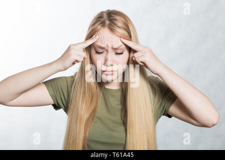 Jeune femme la pensée, les doigts sur les tempes, essayant de se souvenir de quelque chose, sur le fond gris. Banque D'Images