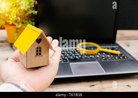 Searching for home concept. Maisons modèles qui sont placés sur la main et des lunettes ont sur les ordinateurs portables. L'arrière-plan est l'écran d'un ordinateur avec espace libre pour Banque D'Images