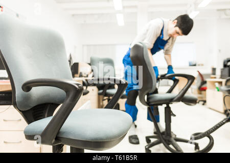 Jeune homme de vêtements et des gants de caoutchouc nettoie la chaise de bureau avec du matériel professionnel. Banque D'Images