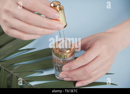 Woman's hand holding pipette avec liquide dans lequel les particules d'or sont visibles. La feuille de palmier dans un arrière-plan. Banque D'Images