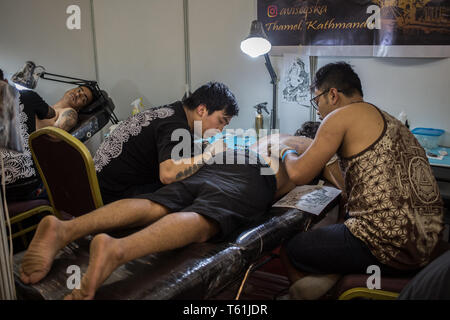 Un homme faire un tatouage de deux artistes sur un stand lors de la convention de tatouage annuel dans la capitale Banque D'Images