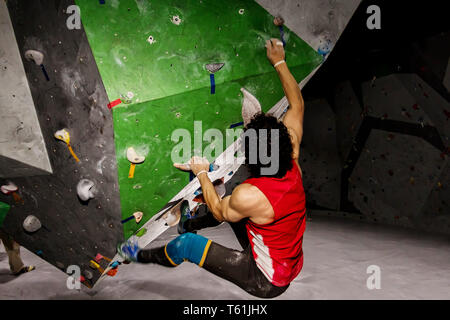 Rock climber hanging man sur un mur d'escalade de bloc, à l'intérieur sur les crochets de couleur Banque D'Images