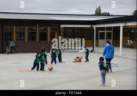 Les petits enfants à jouer dans leur cour d'école à côté de l'église en bois sur Nercon de l'île de Chiloé, Chili Banque D'Images