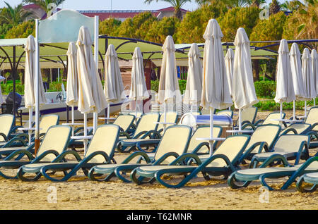 Des chaises vides et fermées des parasols sur une plage de sable Banque D'Images