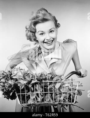 1950 WOMAN RIDING BICYCLE SMILING AT CAMERA VÉLO PANIER PLEIN DE FLEURS - b11030 HAR001 ROSES HARS COPIE ESPACE SANTÉ Mesdames MI-LONGUEUR DE LA CONFIANCE DES PERSONNES TRANSPORT VÉLOS VÉLOS B&W EXPRESSIONS CONTACT DES YEUX BONHEUR JOYEUX JOYEUX SOURIRES LOISIRS FOULARD COU ÉLÉGANT JEUNE FEMME ADULTE NOIR ET BLANC DE L'ORIGINE ETHNIQUE CAUCASIENNE HAR001 old fashioned Banque D'Images