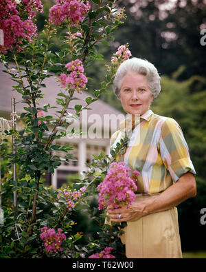 1960 young woman in GARDEN HOLDING CRAPE MYRTLE BLOSSOMS LOOKING AT CAMERA - kb6941 HAR001 HARS SENIOR middle-aged WOMAN EYE CONTACT BONHEUR middle-aged WOMAN ANCIENS LOISIRS EXTÉRIEUR FLEUR ANTIQUE FIERTÉ ANCIENS Fleurs de myrte élégant de la croissance des cheveux gris de l'origine ethnique caucasienne HAR001 old fashioned Banque D'Images