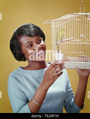 1960 SMILING AFRICAN AMERICAN WOMAN PERRUCHE ANIMAUX DANS UNE CAGE à oiseaux - kb9294 PHT001 AILE CAGE HARS JOYEUX BONHEUR africains-américains africains-américains NOIR ORIGINE CONNEXION JOYEUX SOURIRES Perruche de VERTÉBRÉS À PLUMES à sang chaud jeune adulte ailé BIPÈDE FEMME PONTE des Afro-américains à l'ANCIENNE Banque D'Images