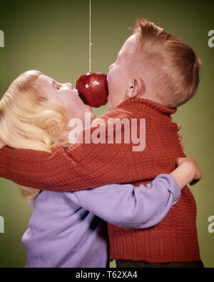 1960 BOY AND GIRL HUGGING TOUT EN ESSAYANT DE MORDRE SUR APPLE STRING PARTY GAME - kj1705 HAR001 FEMELLES HARS BROTHERS STUDIO SHOT ACCUEIL COPIE ESPACE VIE AMITIÉ, mi-longueur Hommes frères soeurs bouchée de bonheur et d'HUMOUR COMIQUE ESSAYER JEU DE PARTIES PENDILLANT FRÈRES MINEURS COOPÉRATION Octobre 31 octobre l'unité de l'origine ethnique caucasienne HAR001 old fashioned Banque D'Images
