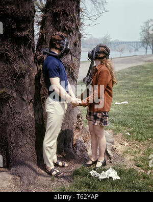 1970 JEUNE COUPLE HOMME FEMME portant des masques à gaz en tenant la main de l'arbre sur le sol de la litière - KS6905 HAR001 HARS, BANDE DESSINÉE JEUNES ADULTES FEMELLES VIE POLLUTION SÉCURITÉ NATURE MASQUE COPIE ESPACE AMITIÉ MASSE pleine longueur PERSONNES CHERS TRISTESSE SOUFFLE RISQUE DE CATASTROPHE SMOG BIZARRE BIZARRE DE RESPIRER LA PROTECTION DE L'ENVIRONNEMENT RELATIONS NON CONVENTIONNELLES LOUFOQUES CONCEPTUELS CONNEXION LITIÈRE ÉCOLOGIE WACKY STYLE AMUSANT IDIOSYNCRASIQUES EXCENTRIQUE COOPÉRATION YOUNG ADULT MAN WOMAN LA POLLUTION DE L'atmosphère de l'AIR MAUVAISE ETHNICITÉ CAUCASIEN HAR ERRATIQUE001 old fashioned toxiques scandaleux Banque D'Images