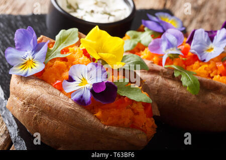 L'igname cuite au four avec du fromage à la crème décoré de fleurs comestibles close-up sur la table horizontale. Banque D'Images