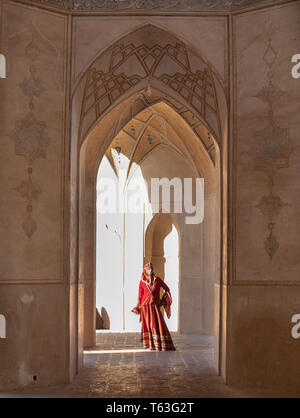 Belle jeune femme iranienne habillés en costume traditionnel rouge dans une mosquée à Kashan Banque D'Images