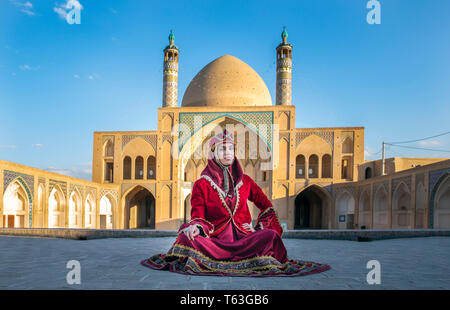 Belle jeune femme iranienne habillés en costume traditionnel rouge dans une mosquée à Kashan Banque D'Images
