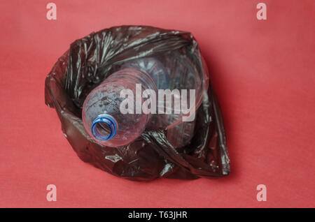 Transparent en plastique bouteille vide dans un sac noir dans un récipient sur un fond rouge avec l'espace pour le texte. Concept de la pollution par le plastique Banque D'Images