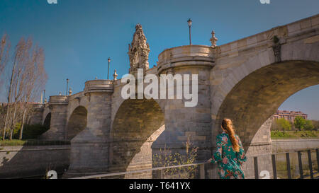 Une jeune femme se tient debout en face de l'ancien pont de Tolède médiévale calcaire ou Puente de Toledo centre-ville de Madrid, Espagne à Madrid Rio Park Banque D'Images