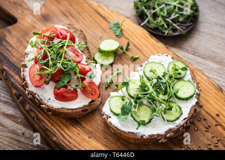 Des toasts avec du fromage blanc, concombre, tomate cerise et microgreen sur planche de bois. Entrée ou en nourriture du petit déjeuner Banque D'Images