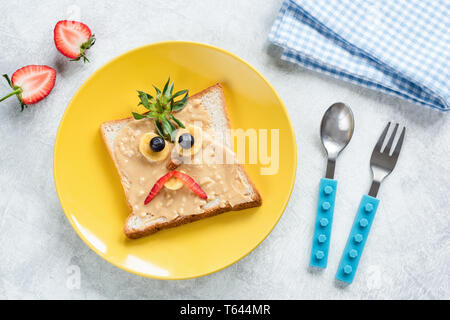 Petit-déjeuner enfants sandwich avec du beurre d'arachide et drôle de visage décoration sur une plaque jaune. Vue de dessus de table. Cuisine créative de l'art, la nourriture saine Banque D'Images