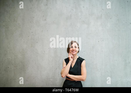 Un portrait of young cheerful businesswoman standing in office, la pensée, l'espace de copie. Banque D'Images