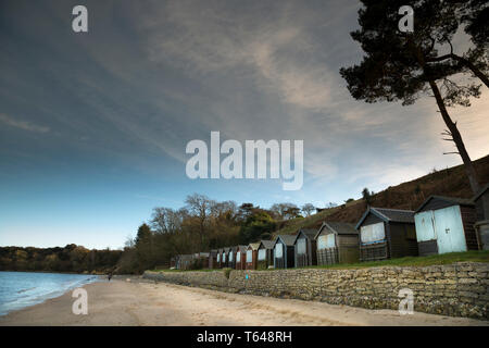 Rangée de cabanes de plage, fermée pour la saison d'hiver sur une plage britannique déserte. Promeneur de chiens isolé sur le rivage, South Beach Studland, Dorset, Royaume-Uni Banque D'Images