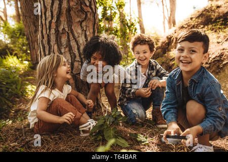 Groupe d'enfants mignons assis ensemble dans la forêt et à la recherche à l'appareil photo. Mignon enfants jouant dans les bois.
