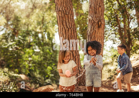 Les filles se ferme les yeux tout en éclatant des ballons d'eau. Les gouttelettes d'eau volent dans l'air et les enfants s'amuser dans le parc. Banque D'Images